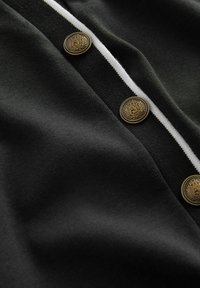 Black fabric with a smooth texture, featuring white stripes and gold-tone buttons with an embossed design, arranged along the front.