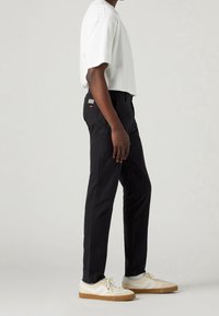 Pantaloni neri con taglio dritto, abbinati a una maglietta bianca. Caratteristiche includono tasche laterali e un'etichetta con il marchio sul retro.
