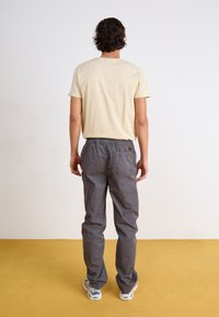 Lyse beige bomull T-skjorte med korte ermer, kombinert med grå bukser med elastisk liv som har en baklomme og en subtil merkevaredetalj.