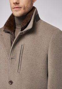 Cappotto in misto lana marrone con colletto foderato in pelliccia, dotato di una tasca con zip e chiusura a bottone, tessuto testurizzato e vestibilità sagomata.