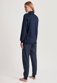 Marineblauwe lange mouwen top en pyjamabroek met stippen. Zachte stof, relaxte pasvorm, taps toelopende enkelmanchetten en een eenvoudig kraagontwerp.