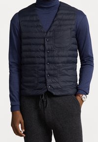 Granatowa kamizelka puchowa z przeszytymi poziomymi panelami, czterema zatrzaskami i dwoma przednimi kieszeniami; założona na granatowy golf.