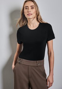 Sort kortærmet t-shirt lavet af glat stof med rund halsudskæring, parret med højtaljede, taupe bukser med knapdetaljer.