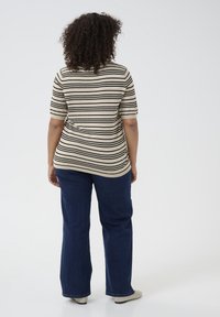 Top de rayas beige y negro con mangas cortas, combinado con jeans rectos de pierna oscura y calzado de color claro.