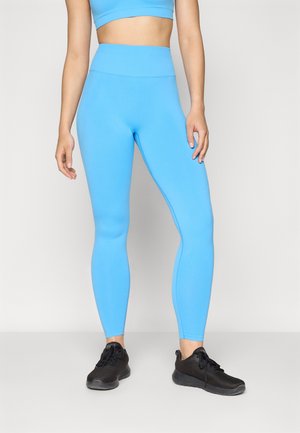 Lyseblå leggings laget av elastisk stoff, med høy midje og en slank, tettsittende design, kombinert med svarte treningssko.