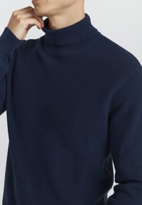 Mornarsko rebrasto pulover s turtleneck ovratnikom in teksturiranim pletenim vzorcem. Ima dolge rokave in sproščen kroj.