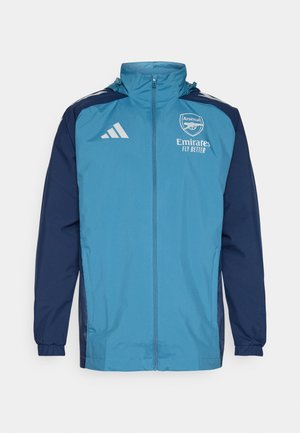 Leichte, wasserdichte Jacke mit einer türkisfarbenen Front und navyblauen Ärmeln, ausgestattet mit einem Reißverschluss, Kapuze und Logo-Akzenten auf der Brust.