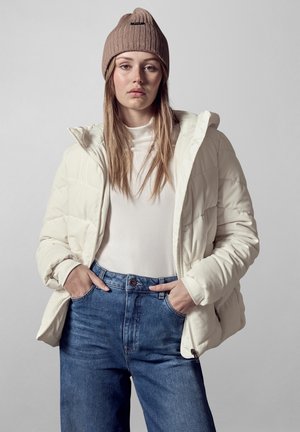 Puffy witte jas met een capuchon, textuurstof, gedragen over een crèmekleurig topje en blauwe jeans. Bruine gebreide beanie voegt warmte toe. Eenvoudige, strakke lijnen.