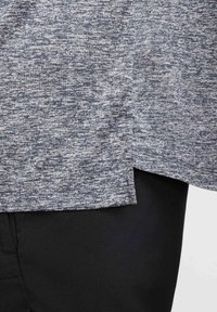 Top de manga corta en gris jaspeado con tejido texturizado, con un corte recto y aberturas laterales, combinado con pantalones negros.