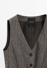 Veste sans manches en lin gris avec un col en V profond et deux boutons noirs, étiquetée Massimo Dutti, fabriquée au Maroc.