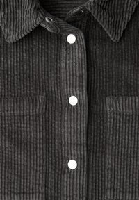 Grijs corduroy overhemd met kraag, knoopsluiting aan de voorkant en twee opgestikte zakken, met een opvallende verticale geribbelde textuur en witte knopen.