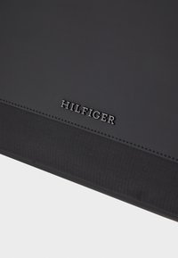 Czarny portfel wykonany z syntetycznego materiału z wytłoczonym logo "HILFIGER", z teksturowanym akcentem i gładką powierzchnią dla eleganckiego wyglądu.