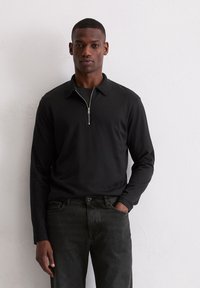 Zwart poloshirt met lange mouwen en een ritssluiting bij de kraag, gecombineerd met donkere jeans. Gladde textuur en nauwsluitend ontwerp, geschikt voor casual draagstijl.