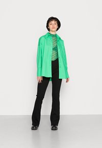 Camisa verde, blusa de padrão transparente, calças pretas largas e calçado preto. Projetado com um corte descontraído e um contraste de cores proeminente.