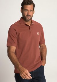 Polo di colore arancione bruciato con colletto e maniche corte. Presenta un piccolo logo "JP" di colore chiaro sul petto. Tessuto di cotone morbido.