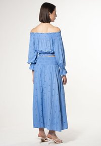 Lichtblauw off-shoulder top en maxi rok set, met een smocked taille en geborduurde patronen. Lange mouwen met gerimpelde manchetten.