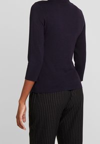 Granatowy sweter dzianinowy z wysokim kołnierzem, rękawami do łokcia i dopasowaniem w talii, zestawiony z czarnymi spodniami w cienkie paski.