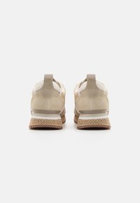 Beige sneakers featuring a textured upper, padded collar, and rope-like accents on the midsole. Minimalist design with a soft finish.