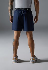 Marine sports shorts med elastisk talje, der har teksten "PIER ONE SPORT". Modellen bærer grå og guld atletik sko.