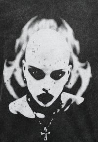 Άτομο φαλακρό με σκούρο μακιγιάζ ματιών και κραγιόν, φοράει κολιέ ανκ, με ένα στυλιζαρισμένο φλόγα ή αφηρημένο σχήμα πίσω από το κεφάλι.