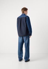 Denim striukė su tamsiu audinio plotu nugarinėje pusėje. Didelės kišenės ir laisvo kirpimo džinsai. Šviesiai skalbti, su klasikiniu pjūviu.