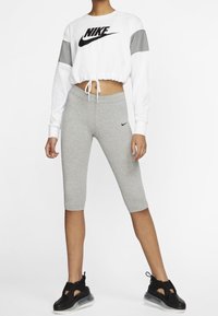 Vit croppad sweatshirt med grå ärmmärken och en svart logo, tillsammans med grå leggings och svarta sportskor med genomskinliga sulor.