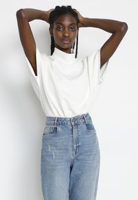 White short-sleeve top with a high collar, paired with light blue high-waisted jeans featuring distressed details and a straight-leg fit.