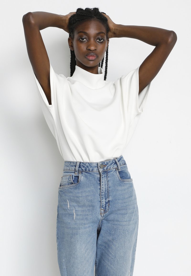 White short-sleeve top with a high collar, paired with light blue high-waisted jeans featuring distressed details and a straight-leg fit.