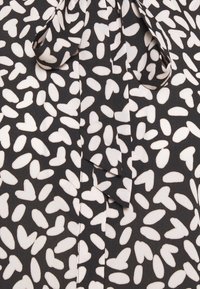 Tissu noir avec des motifs irréguliers en forme de cœur blanc et des ovales, avec un détail de nœud noué au centre.