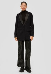 Black blazer with satin shawl lapel, two front pockets, paired with shiny black sequin pants and platform shoes.