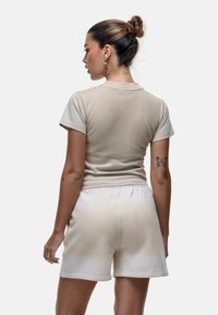 T-shirt in cotone beige con maniche corte, abbinata a pantaloni corti beige chiaro. L'outfit presenta una vestibilità comoda e cuciture minime.