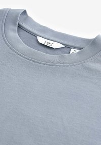 Tricou lejer de culoare gri deschis, cu guler rotund, fabricat dintr-un material moale din amestec de bumbac, având o croială relaxată. Prezintă cusături simple și eticheta brandului în interiorul gulerului.