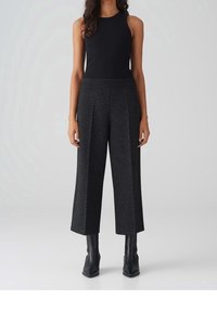 Débardeur noir sans manches associé à un pantalon large taille haute en tissu texturé sombre, complété par des bottines noires à talons pointus.