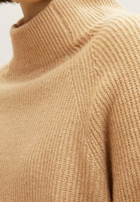 Beżowy sweter dziany z wysokim kołnierzem typu golf. Teksturowany prążkowany wzór, miękka tkanina i luźny krój.