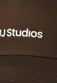 Brah kapica iz teksturirane tkanine s ukrivljenim vizirjem. Na sprednji strani je jasno prikazan bel logotip "AJ Studios".