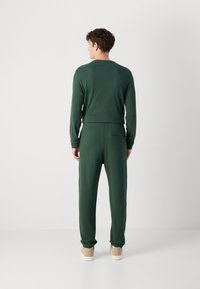 Grønn strikket langermet topp og matchende joggebukser, med et tettsittende liv, en ekstra baklomme og elastiske mansjetter. Brune sneakers.