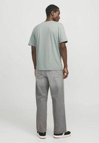 Lysegrøn bomulds t-shirt med afslappet pasform, korte ærmer og rund hals, parret med løse grå jeans og sorte sneakers.