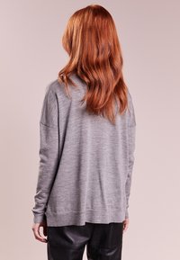 Szary sweter dzianinowy o luźnym kroju, z opadającymi ramionami i prążkowanym wykończeniem, zestawiony z czarnymi skórzanymi spodniami. Minimalistyczny design.