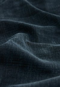 Tela de mezclilla azul oscuro con una textura sutil, que presenta una superficie suave y lisa con un ligero brillo, dispuesta en pliegues suaves y fluidos.