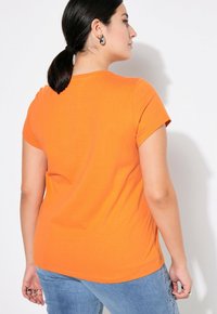 Oranges Baumwoll-T-Shirt mit kurzen Ärmeln und rundem Ausschnitt, von hinten präsentiert, zeigt eine glatte Textur und einen lässigen Schnitt.