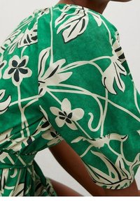 Robe florale verte en tissu léger, avec des motifs botaniques noirs et blancs, manches courtes, et une taille cintrée.