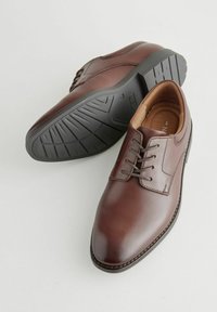 Chaussures de ville en cuir marron avec bouts ronds, design à lacets, couture renforcée et semelles en caoutchouc noir texturé. Fini lisse et profil élégant.