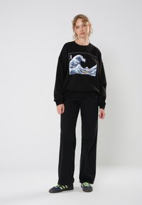 Black sweatshirt featuring a blue and white wave graphic, paired with black pants and blue shoes with green stripes. Simple design and relaxed fit.