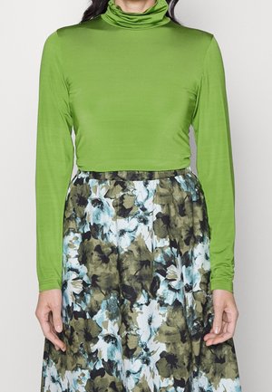 Person wearing a bright green long-sleeve turtleneck tucked into a high-waisted floral skirt with blue, green, and black patterns.