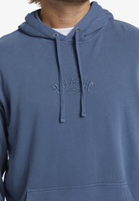 Felpa blu in cotone con cappuccio regolabile, tasca frontale e logo ricamato in un sottile design tonale sul petto.