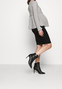 Šedý žebrovaný svetr s rozšířeným lemem, kombinovaný s černou pouzdrovou sukní a černými kotníkovými botami s špičatou špičkou a lesklým zipem.