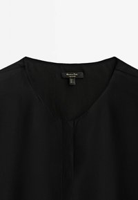 T-shirt noir col V avec patte de boutonnage cachée et petite étiquette de marque à l'arrière du col indiquant les détails de la taille.
