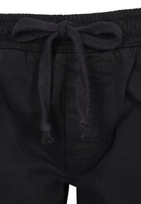 Svarta byxor med en mjuk midjeband, utrustade med en svart snörning och subtila sömnadsdetaljer vid midjan och fickorna.