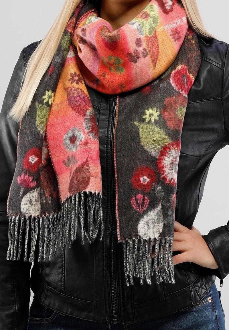 Femme portant une veste en cuir noire et une écharpe fleurie colorée aux extrémités à franges, drapée autour du cou et des épaules.