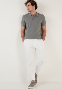 Šedé polo tričko s krátkým rukávem a límečkem, spárované s bílými kalhotami a šedými teniskami. Hladká tkanina, uvolněný střih, minimalistický design.